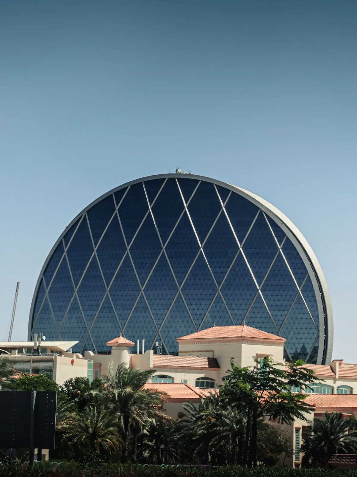 Aldar HQ, the round glass tower at Al Raha Beach, above palm trees and low buildings