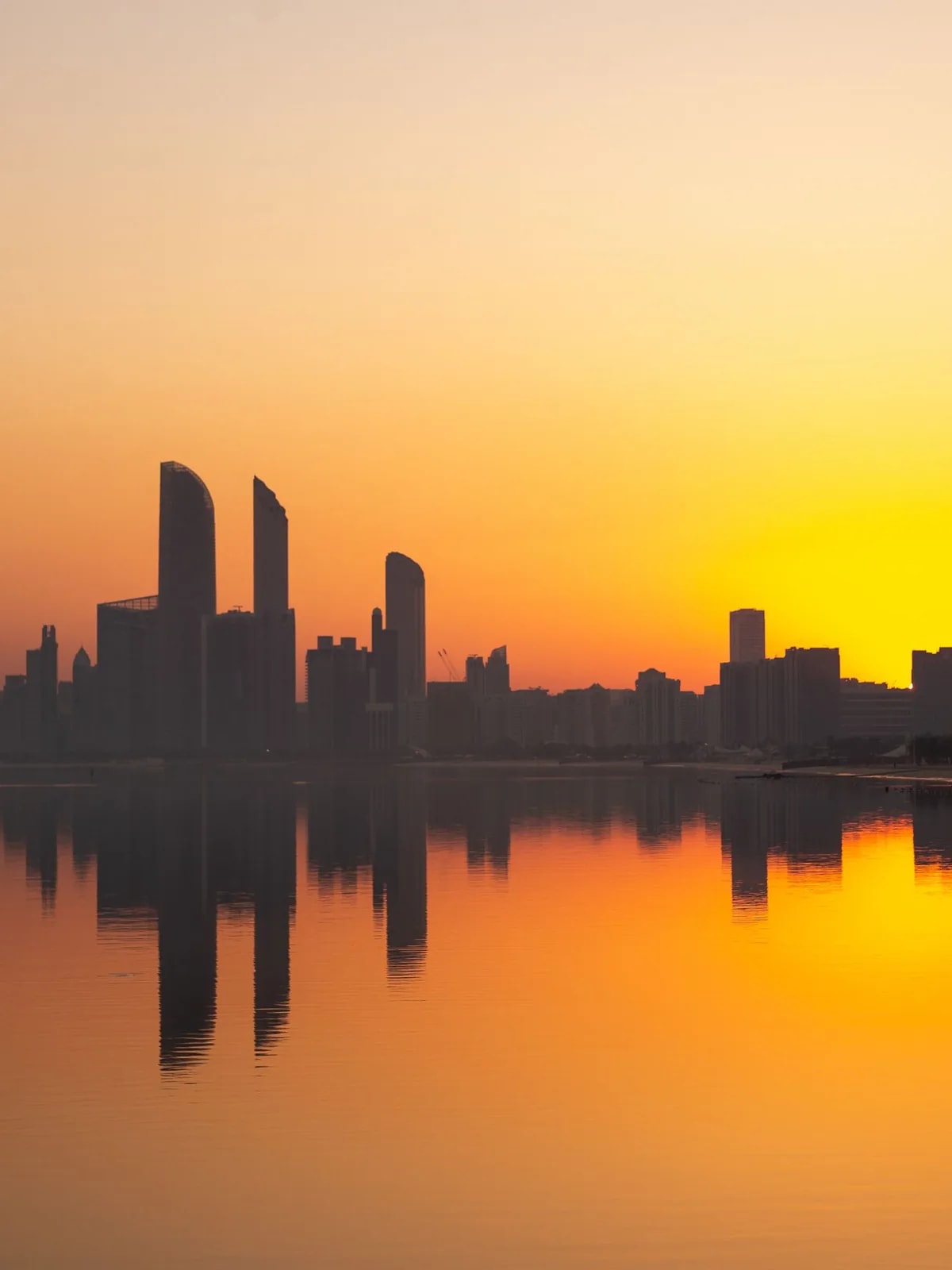 Abu Dhabi towers mirrored in water at sunset, like Al Reem Island’s high-rise homes