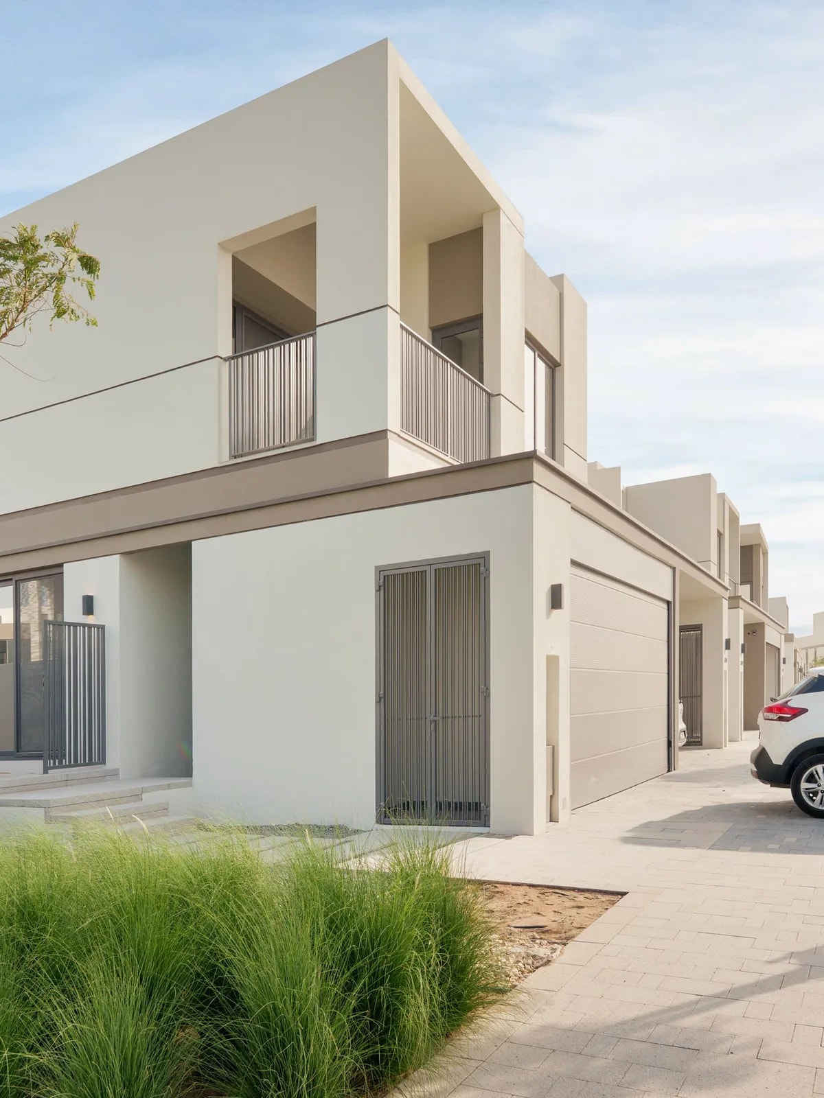 Modern two-storey townhouse with a driveway and young trees, like the DAMAC Hills homes we automate