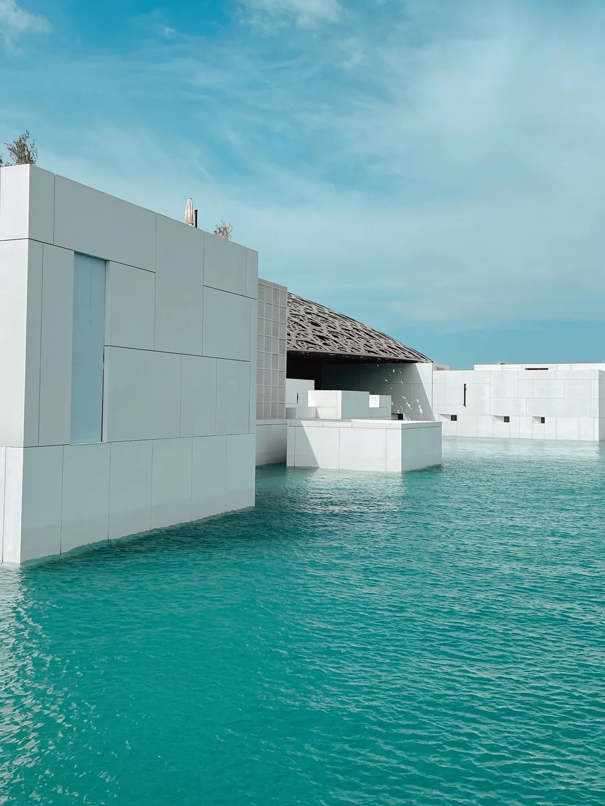 White galleries and dome of the Louvre Abu Dhabi over still turquoise water on Saadiyat Island