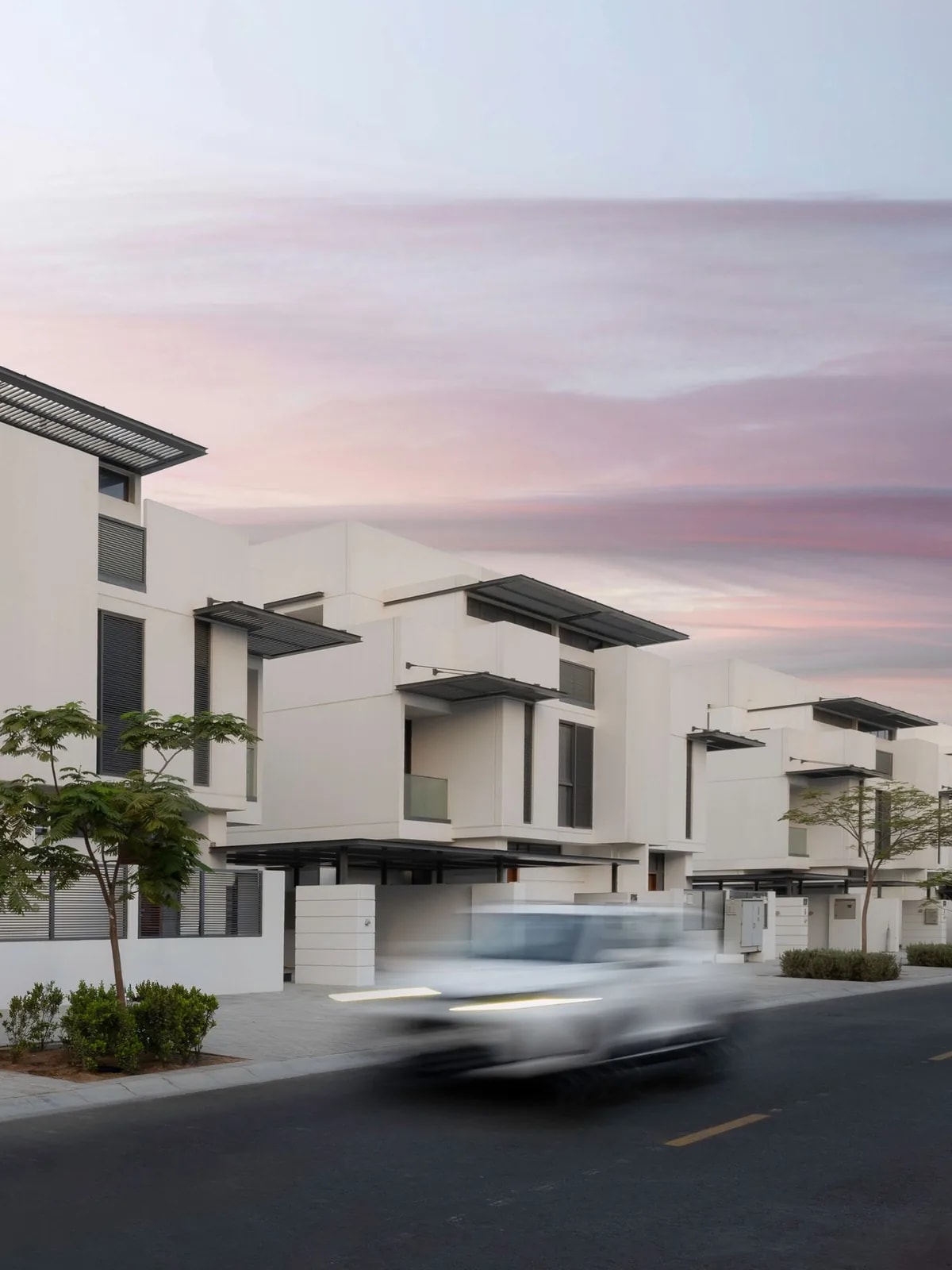 White three-storey townhouses with louvred canopies at dusk, like the townhouses in The Valley we automate