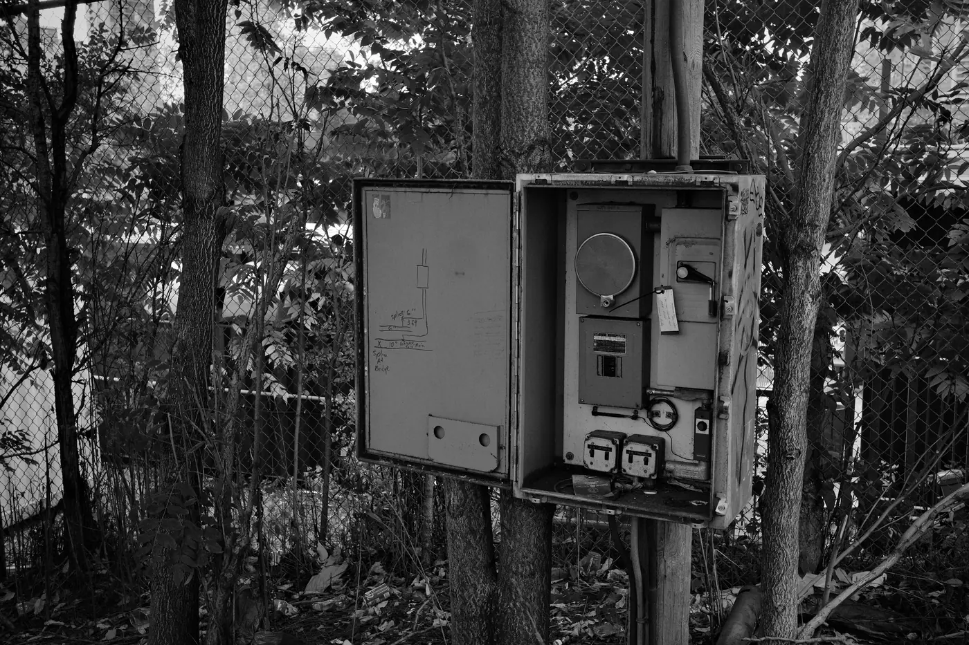 Black-and-white photo of an open outdoor electrical box with a meter and switches, mounted on a pole