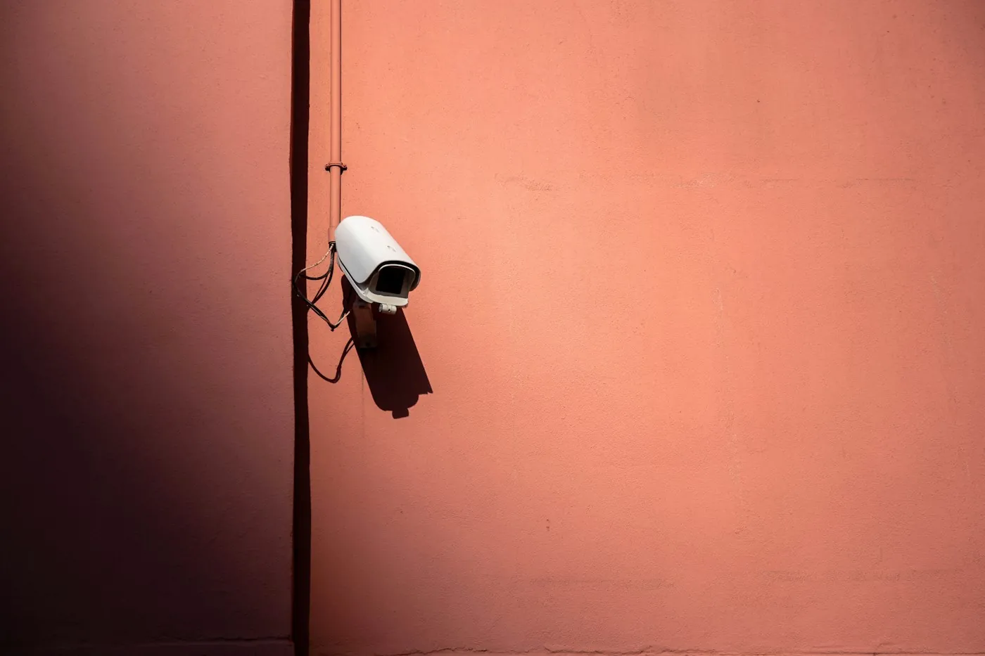 White bullet security camera mounted on an unshaded exterior wall in harsh sun