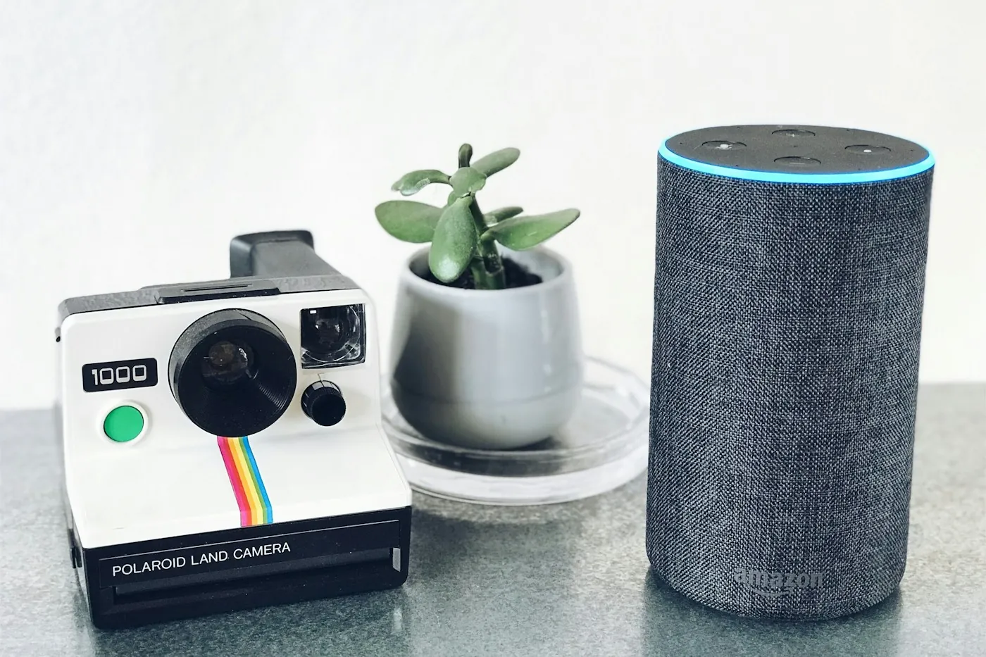 A dark grey Amazon Echo speaker with its blue voice-activation ring lit, on a kitchen counter