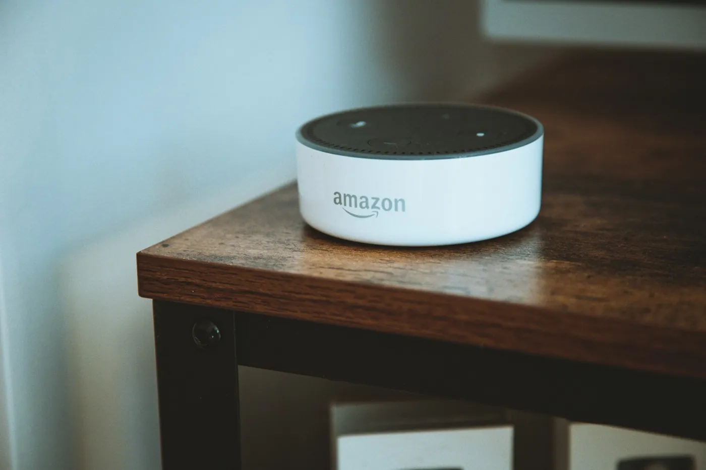 A white Amazon Echo Dot speaker sitting on a wooden side table in a warm-toned apartment