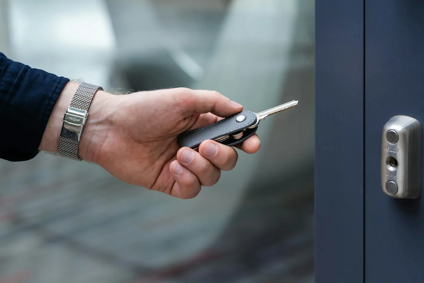Hand using a key at a modern electronic door lock on a dark apartment door