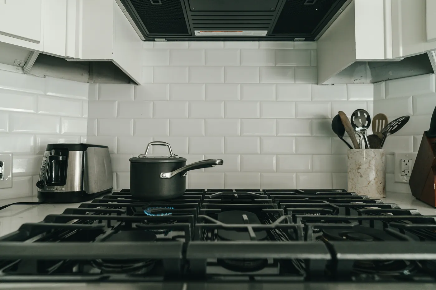 Pot on a lit gas hob in a white-tiled kitchen, the room where the Hassantuk kit uses a heat detector instead of a smoke detector