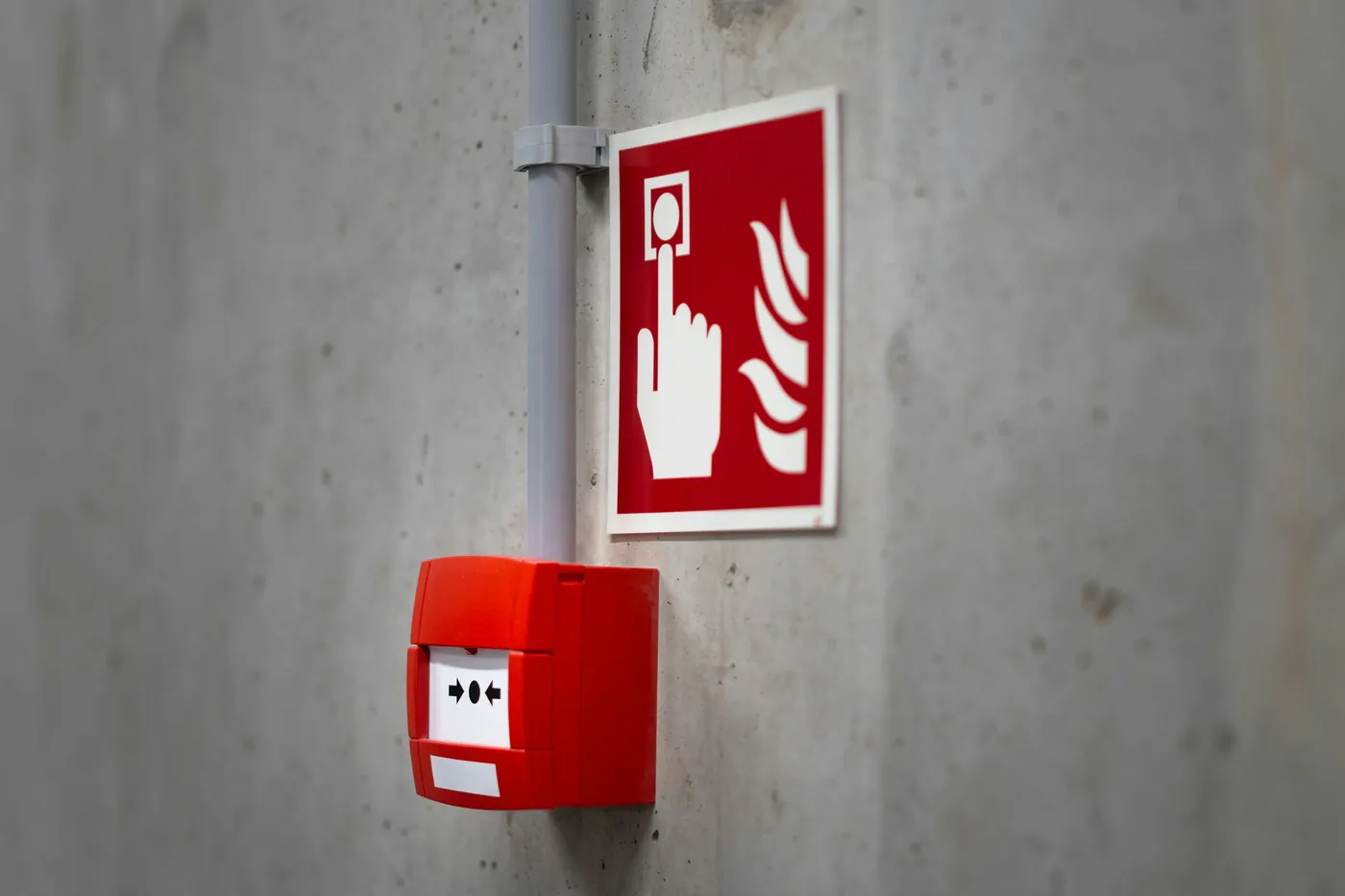 Red manual fire alarm call point and a red fire alarm sign on a grey concrete wall