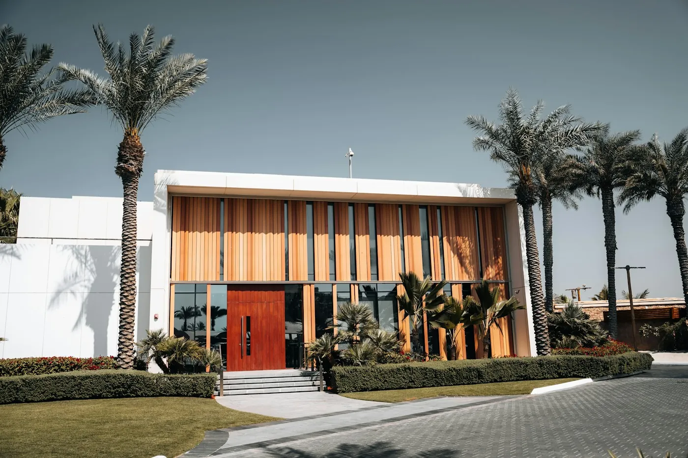 Large modern villa with a timber slat facade and palm trees lining the driveway