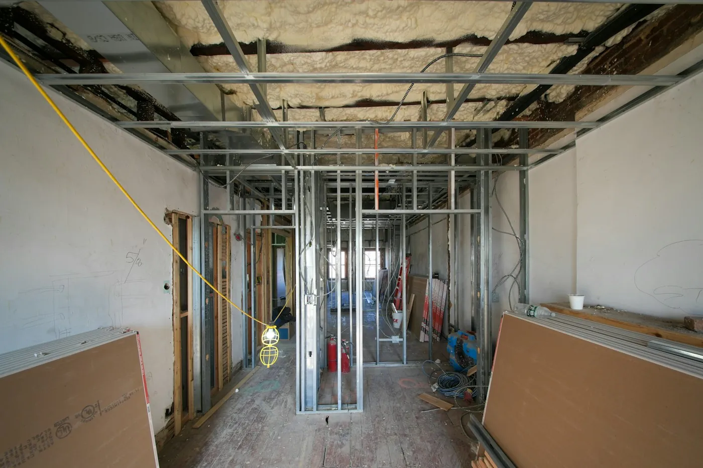 Room mid construction with metal stud framing, ceiling insulation and drywall sheets stacked for installation