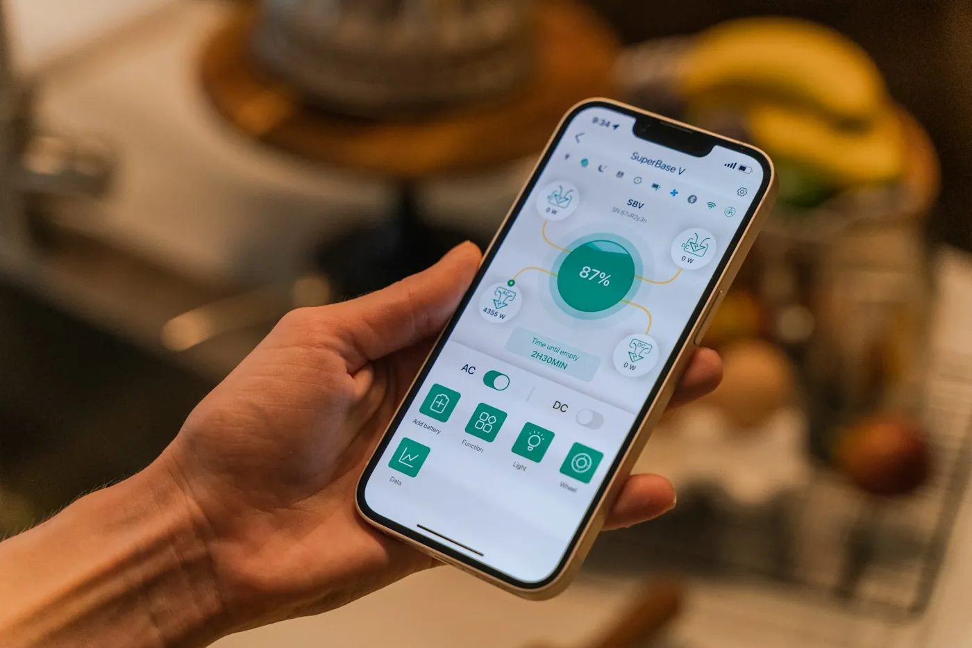 Hand holding a phone open to a smart device control app with a Light button visible, kitchen in background