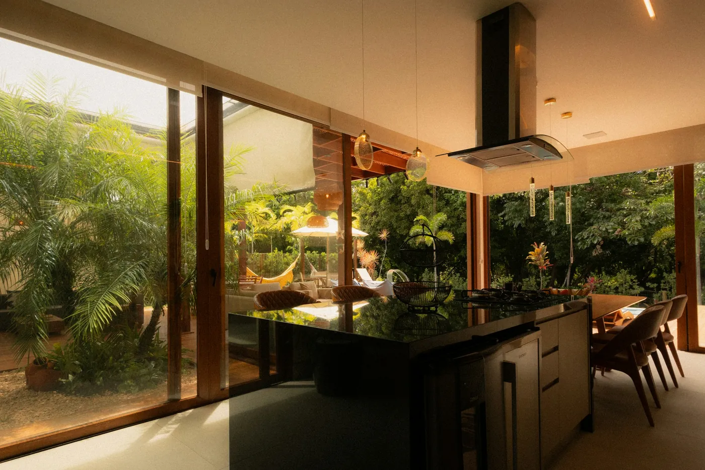 Modern villa kitchen with a dark island, glass pendant lights and tall glass doors opening onto a garden
