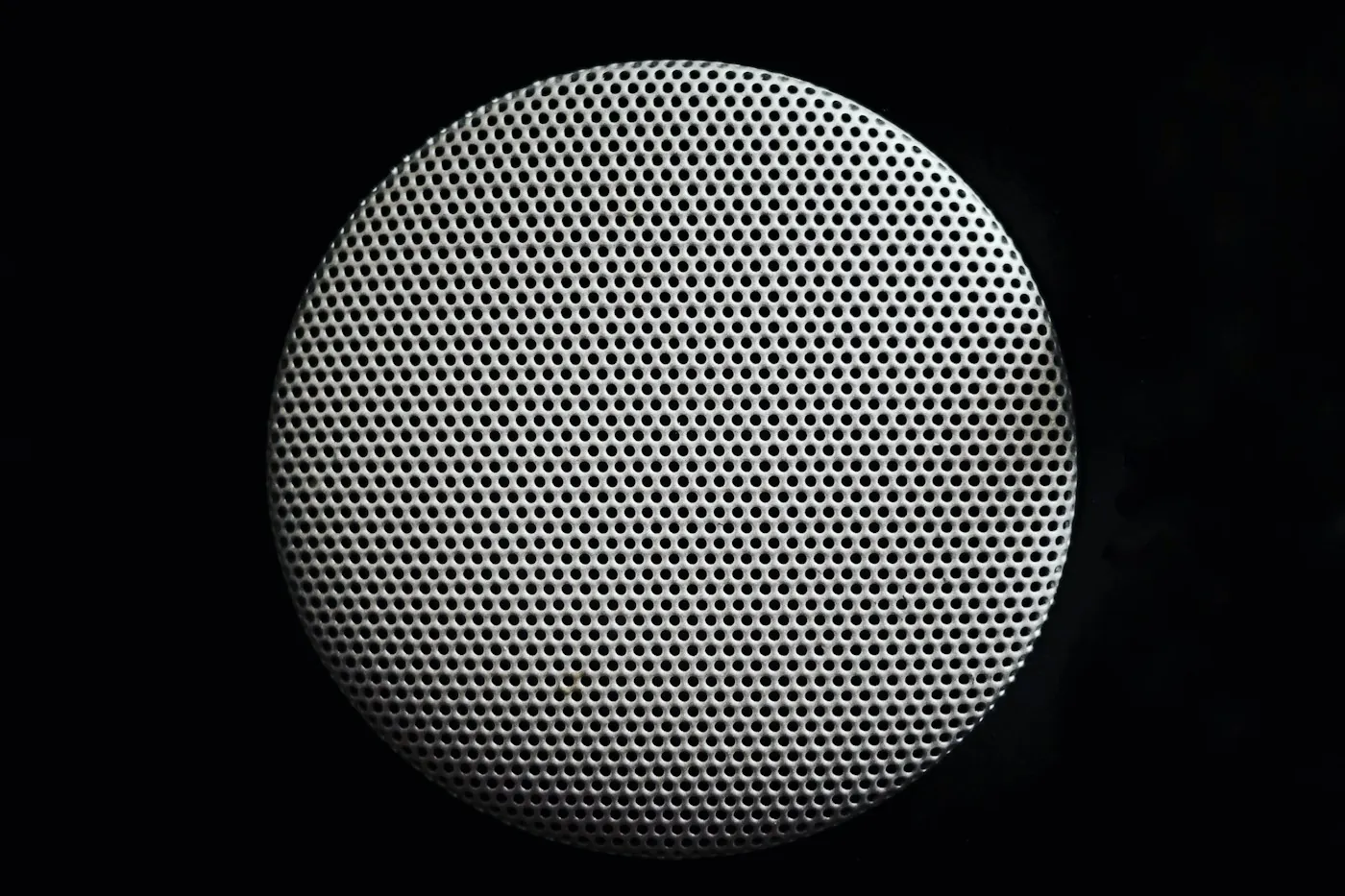 Close-up of a round perforated speaker grille set flush into a surface