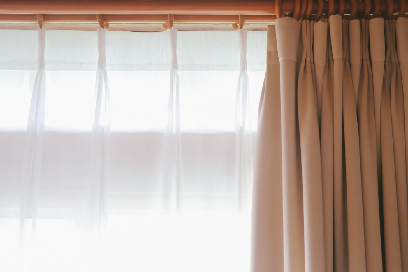 White sheer curtain and beige pleated blackout curtain hanging from rings on one curtain rod
