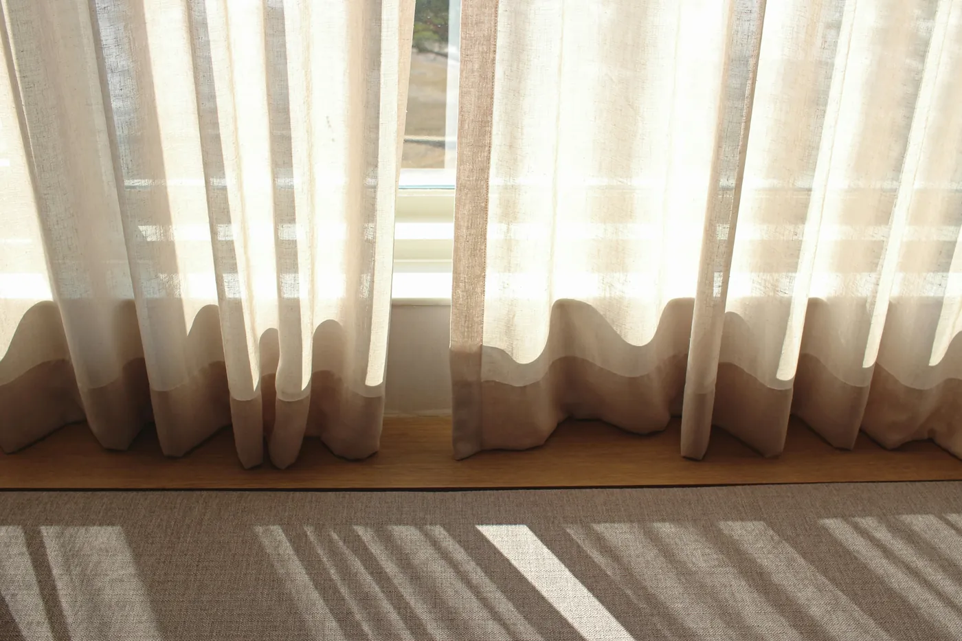 Strong sunlight through white sheer curtains casting window shadows on the floor