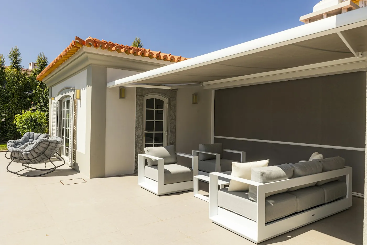 A motorized retractable awning extended over a villa terrace lounge seating area in daylight