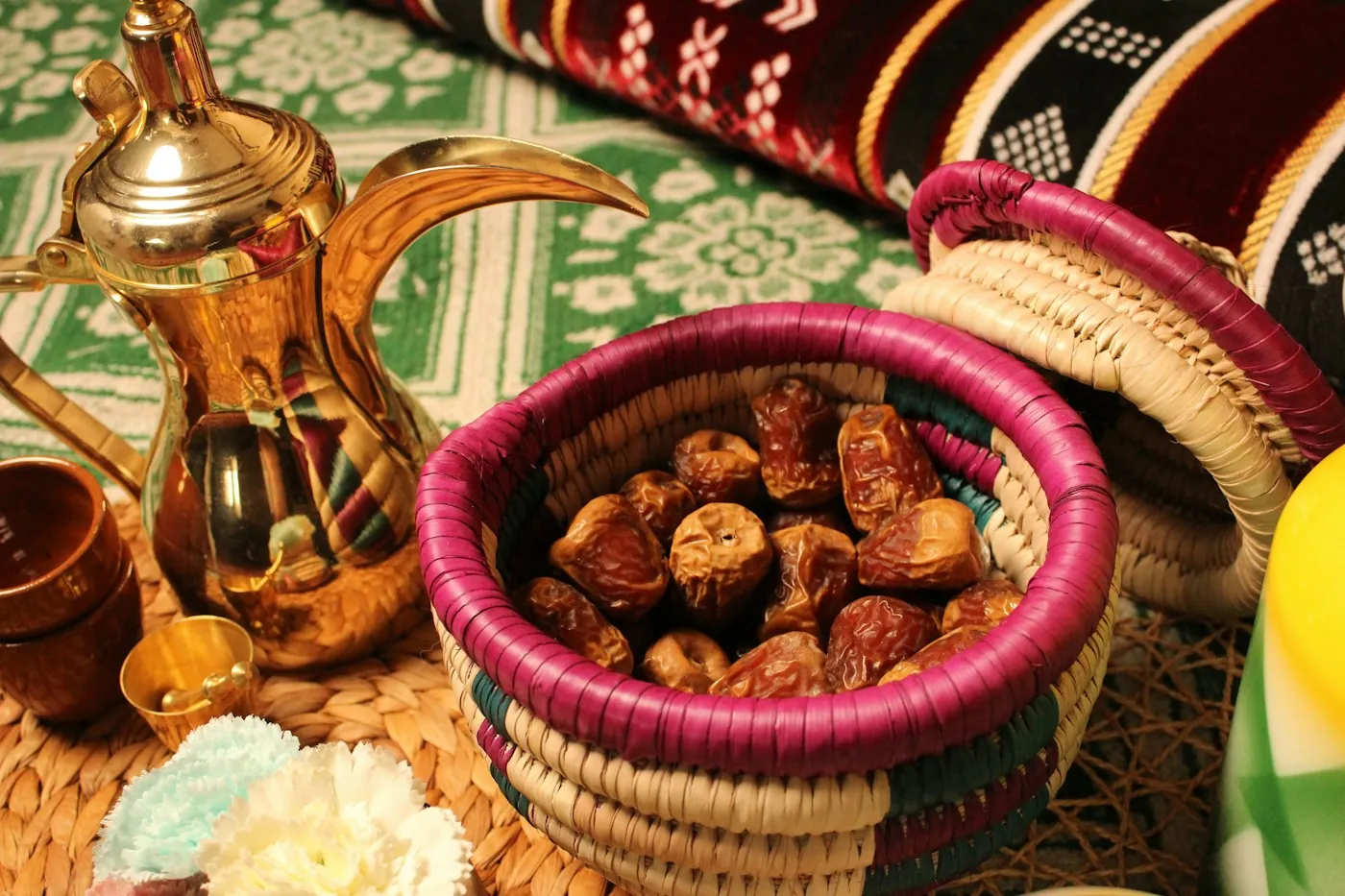 A traditional brass Arabic coffee pot and a woven basket of dates on a patterned rug