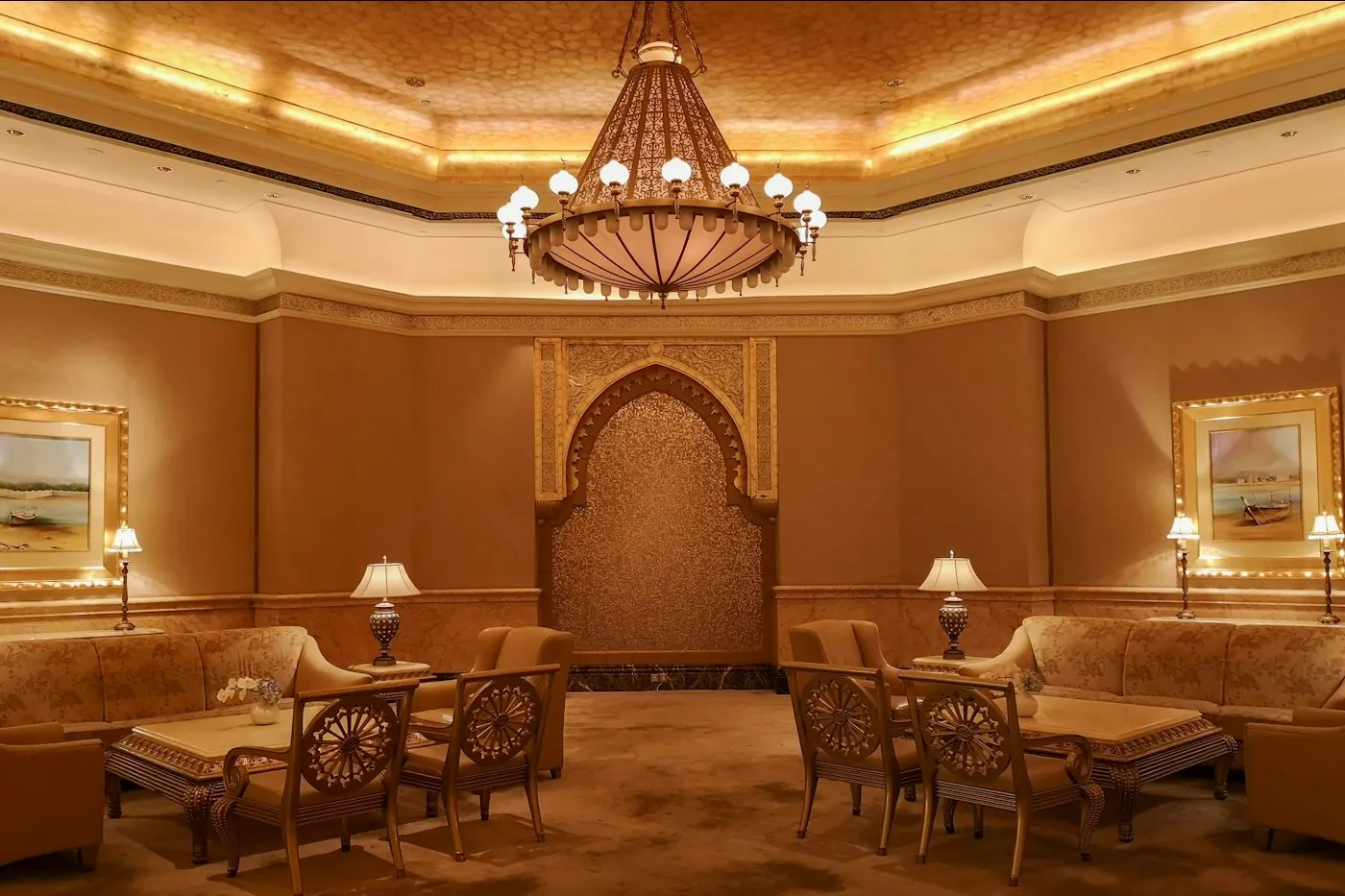 A majlis-style seating area with ornate arched wall, chandelier and warm lamplight