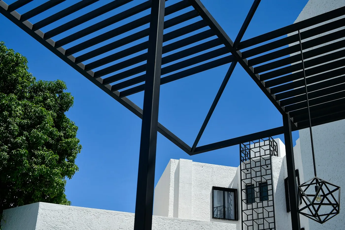 Black louvered pergola shading a villa terrace with an Arabic style lattice screen against a clear blue sky