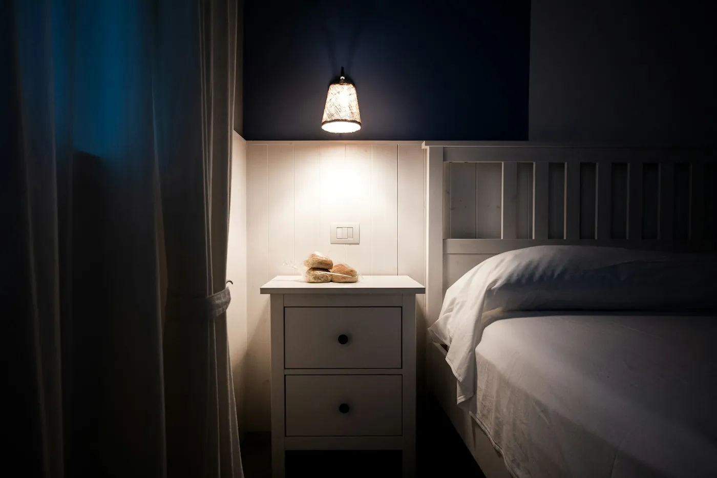 A warm bedside lamp glowing softly beside a bed at night, no camera in view