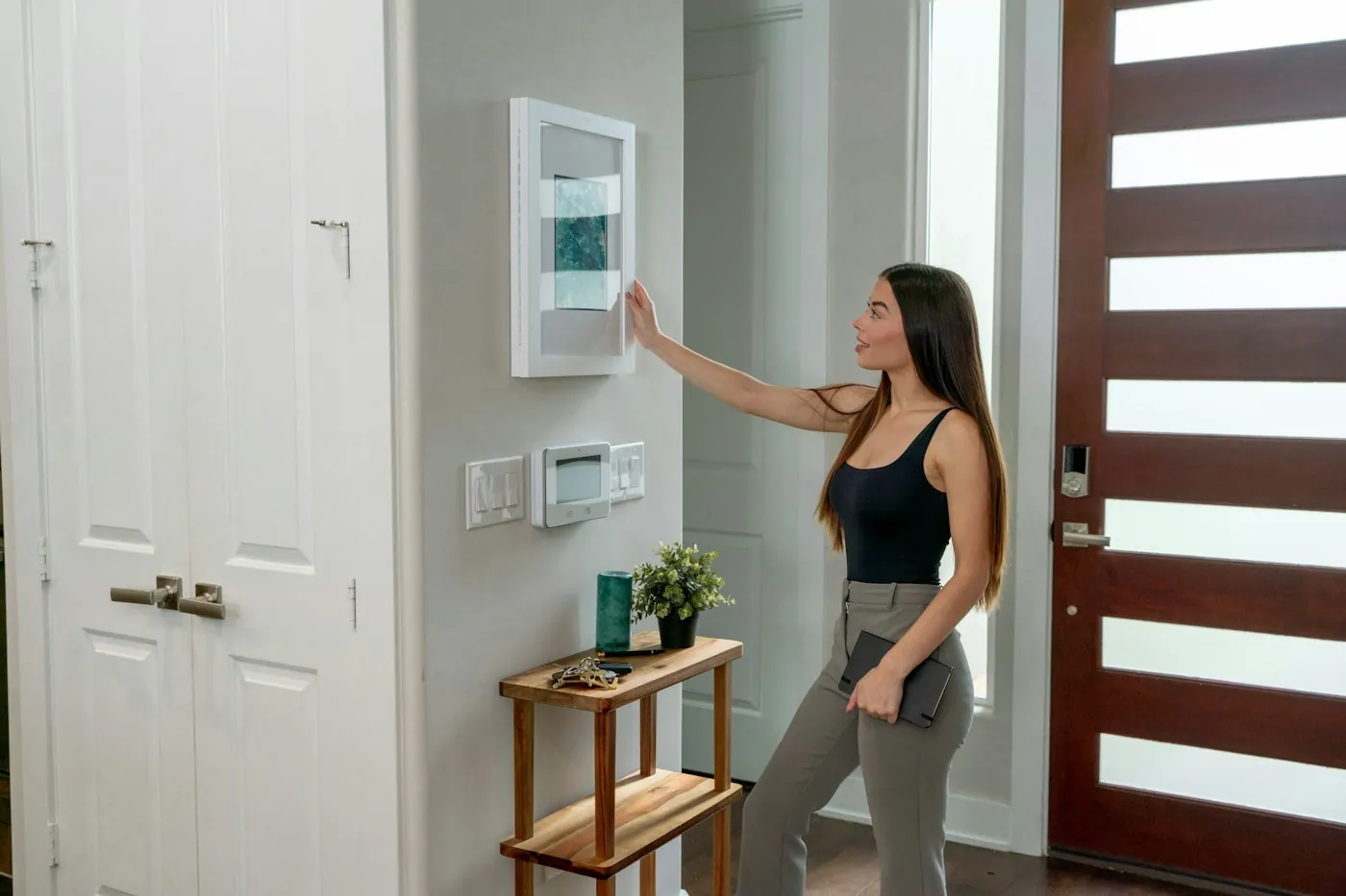 Woman in a modern entryway adjusting a wall-mounted smart control panel