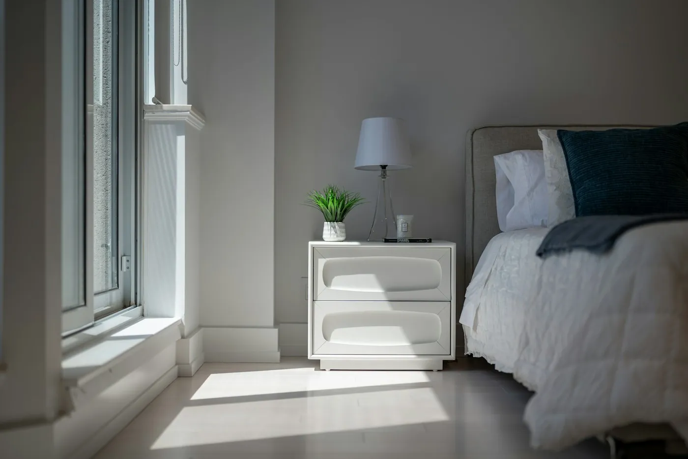Sunlight streaming into a bedroom with a nightstand lamp beside the bed