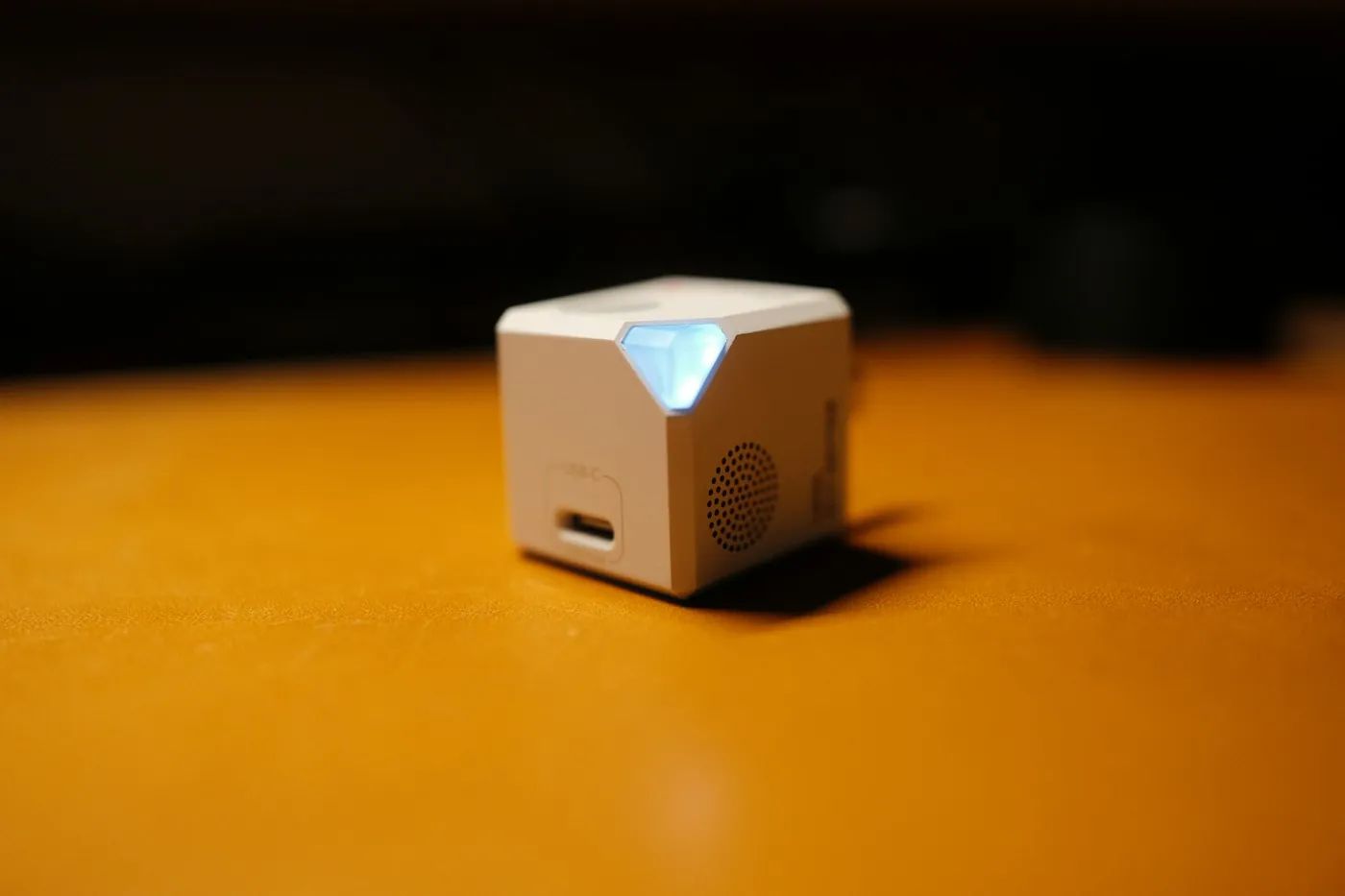 Small white smart home hub device with a glowing status light sitting on a wooden table