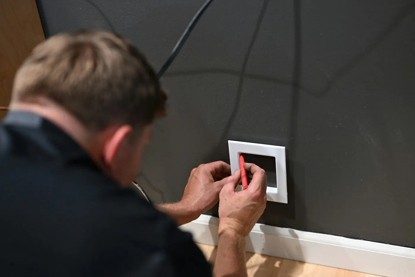 Electrician wiring a wall-mounted device with exposed cabling behind an open wall plate