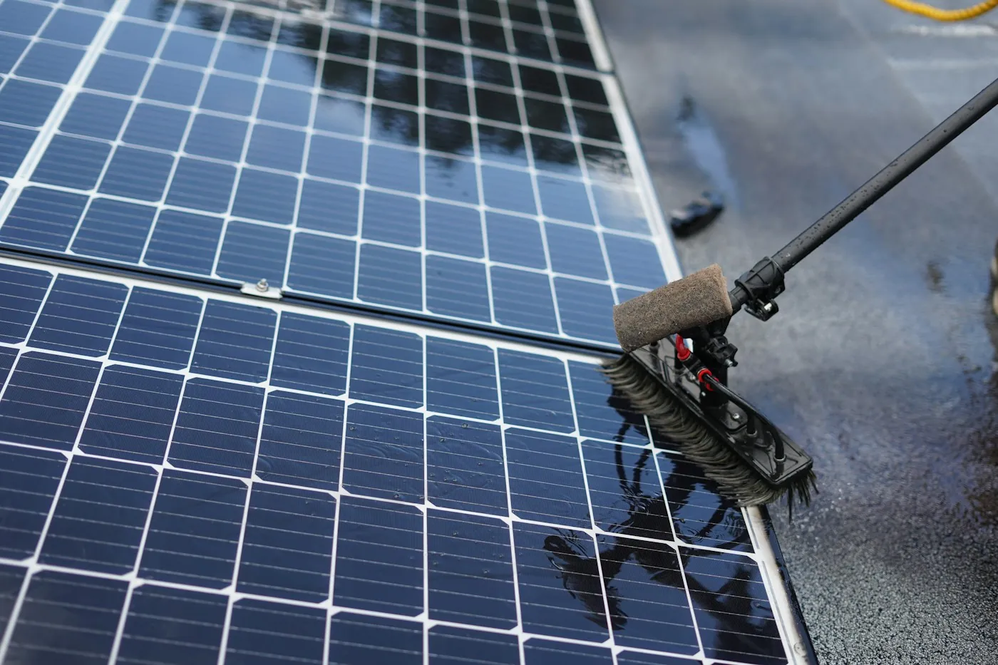 Cleaning a rooftop solar panel array with a long handled brush under a clear sky
