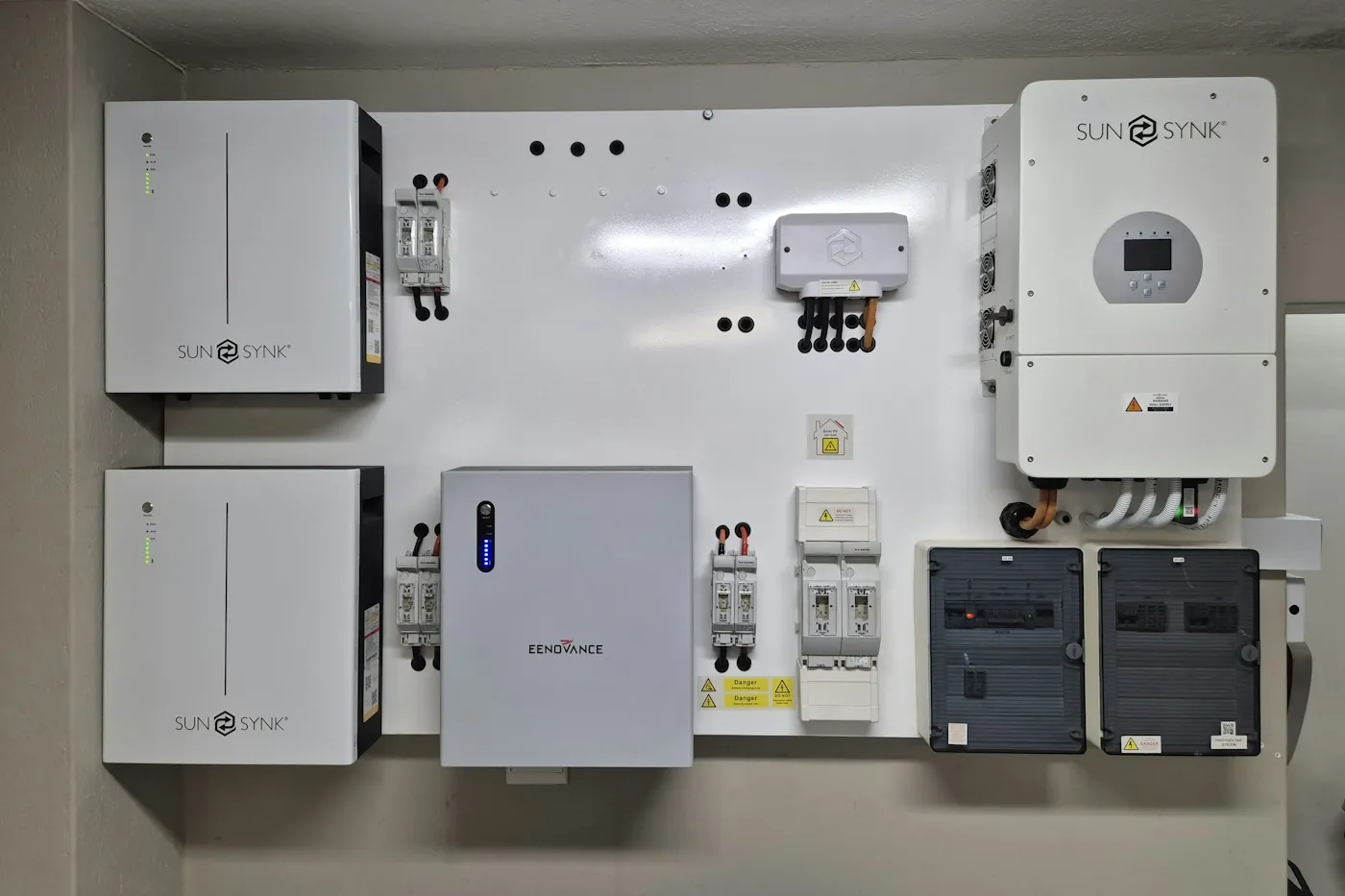 Wall-mounted solar inverter and battery storage units with a small monitoring display, installed in a plant room
