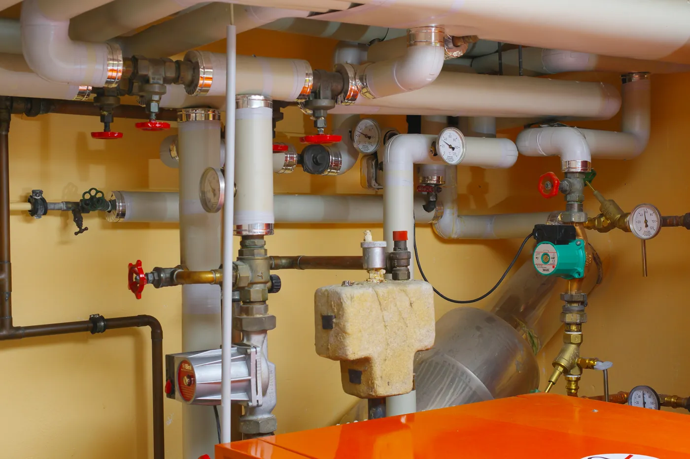 White water pipes with red valve handles, pressure gauges and a hot-water unit in a plant room, all common water leak points
